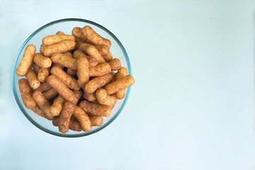 sweet corn sticks among with cocoa in a glass round bowl on a light blue background , top view . gluten free foods for kids