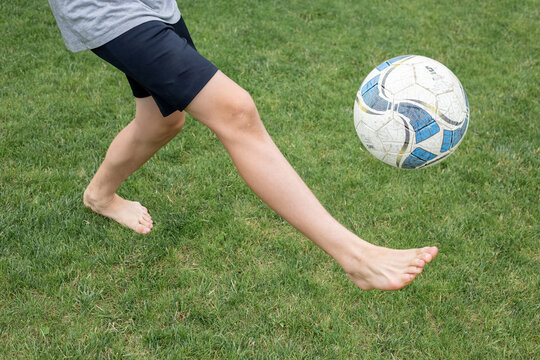 Footballer barefoot stuffs the ball on the green grass.