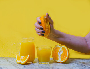 Woman squeezing fresh orange juice in a glass. Yellow background. Summer concept