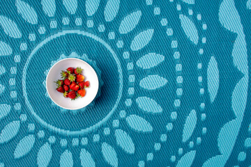 Abstract food background with strawberries in white bowl and colourful patterned turquoise rug. 