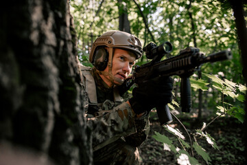 Army soldier in camouflage sitting in an ambush in the forest often hiding behind a tree
