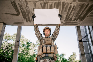Protesting military soldier in camouflage holding up a poster above himself riots against, a...