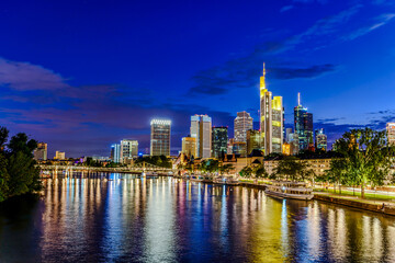Frankfurt am Main. European finance center city downtown skyline cityscape. Eiserner steg bridge, river during twilight blue hour, sunset, evening, night. Gold yellow color. Travel in Hesse, Germany.