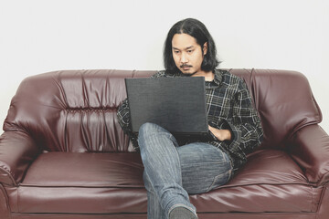 long hair men working on laptop computer sitting on sofa at home