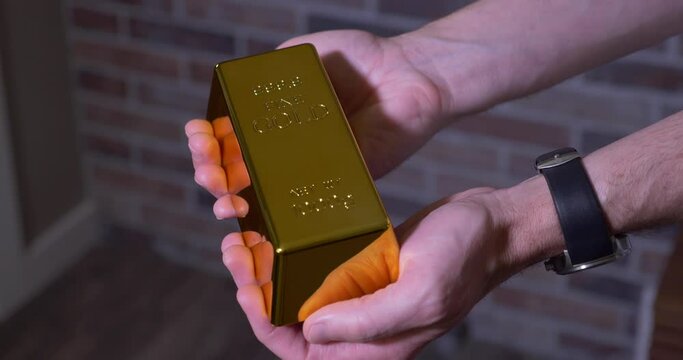 A man holds a single bar of gold.  	