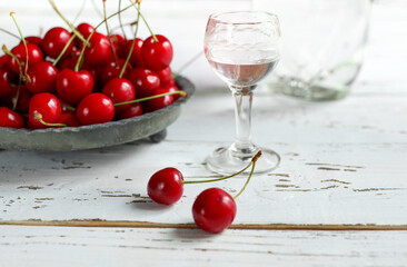 Strong alcoholic cherry drink Kirsch or Kirschwasser -  in a glass and fresh cherry on the white wooden table