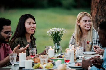 Young intercultural females talking to their boyfriends by served table outdoors