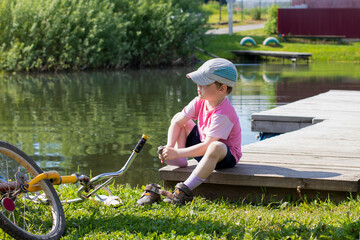 The child takes off his shoes and socks to swim in the pond, throwing an old bicycle nearby.