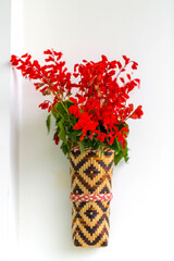 Bamboo flower vase with red lilac flowers hanging on the white wall. Isolated background.