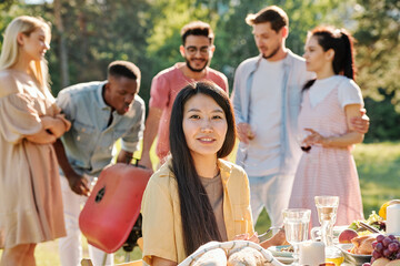 Happy young Asian woman with long dark hair looking at you by served table