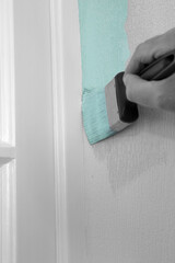 Man painting wall with mint green paint on textured wallpaper,  cutting in agoinst door frame.  With selective colour