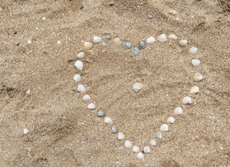Heart made of sea shells laid out on sea sand. Photograph, top view.