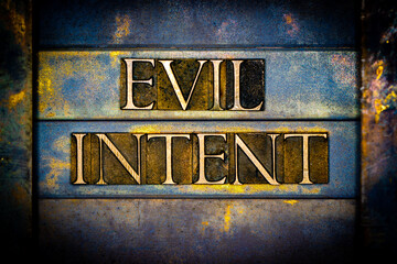 Evil Intent text formed with real authentic typeset letters on vintage textured silver grunge copper and gold background