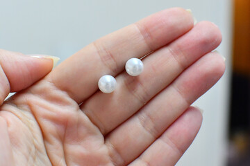 Female hand holding white colored freshwater pearl earring studs