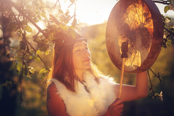 beautiful shamanic girl playing on shaman frame drum in the nature.