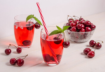 Summer cooling drink with cherries, ice and mint on a white wooden background.