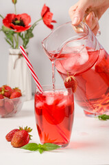 A woman pours from a decanter a summer cooling drink with strawberries and ice.