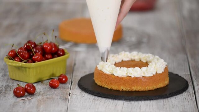 Decorating a cherry cake with cream from the pastry bag.