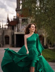 beautiful young woman in long green dress standing posing against the backdrop of a fairytale castle