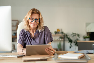 Smiling mature businesswoman using touchpad to surf in the net for online data