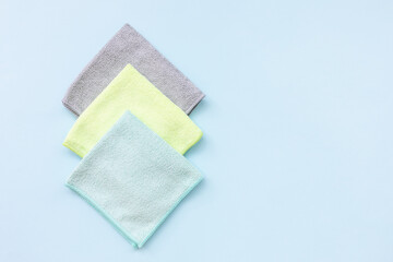 Three new folded microfiber cloth for cleaning over the blue background. Cleaning micro fabric towels for dusting and polishing. Domestic household cleaning service concept. Close up, copy space