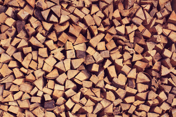 Prepared split and dry firewood for heating. A stacked woodpile. Texture in the form of evenly stacked on top of each other the bars of the tree.