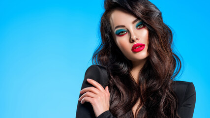 Portrait of beautiful young woman with bright blue makeup.  Pretty girl with long black hair. Brunette woman in a black clothes. Sexy girl. Beautiful brunette with bright red lipstick on her lips..