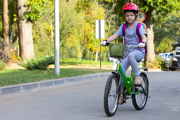 Girl rides a green bicycle in the park in a red helmet.
