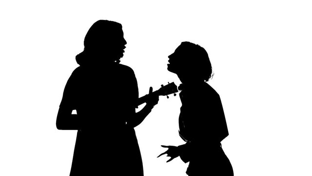 Medium long shot of duet of young talented girls singing and playing ukulele. Creative duet concept. Black silhouette on a white background