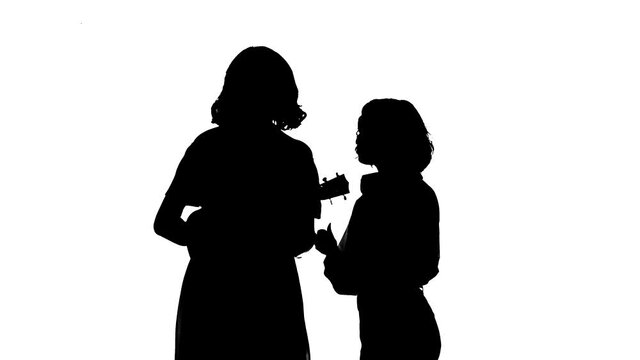 Medium long shot of duet of young talented girls singing and playing ukulele. Creative duet concept. Black silhouette on a white background