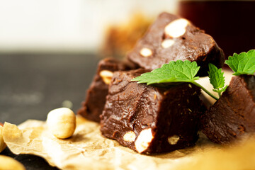 Fondant on craft crumpled paper with nuts and chocolate cubes decorated with green mint leaves. In the background a jar of nuts, blurred background. Sweet composition on a black textural background. 