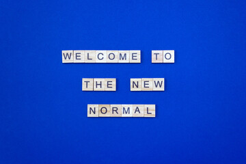 The phrase Welcome to The New Normal made of wooden blocks on blue cardboard background. Layout, top view, place for text.