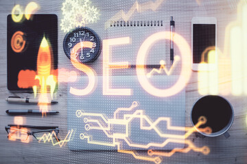 Double exposure of SEO hologram drawing over desktop. Top view. Search optimization concept.