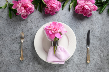 Fototapeta na wymiar Elegance table setting with pink peony, white dishware, silverware on gray. Top view.