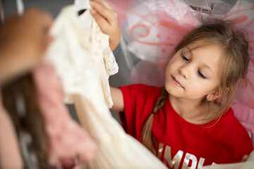 Obraz premium Cute preschooler girl has chosen a new lovely dress among a lot of clothes in child fashion store; she is happy. Sale, gifts, Christmas, holidays; beauty concept, place for your brand on tag