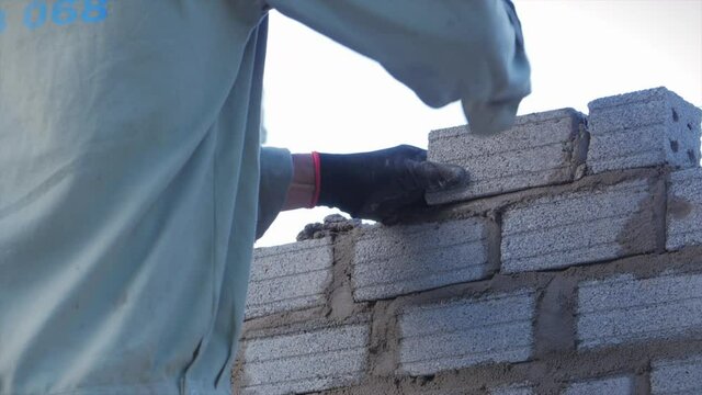 Close shot at the bricklayer's hands, male volunteer worker lays brick into wall with cement using trowel, builder man puts the bricks, using a stretched string for an even level of masonry materials.