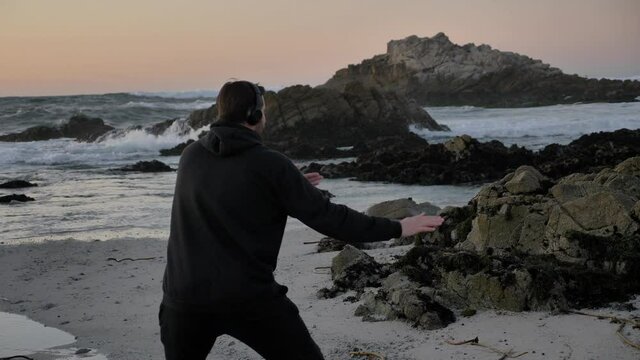 Men warrior monk practicing silhouette tai chi karate kung Fu on the rocky stones horizon at sunset or sunrise. Art of self-defense. Silhouette on a background of dramatic epic waves at pacific coast