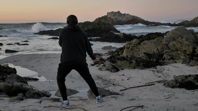 Men warrior monk practicing silhouette tai chi karate kung Fu on the rocky stones horizon at sunset or sunrise. Art of self-defense. Silhouette on a background of dramatic epic waves at pacific coast