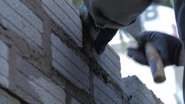 Close shot at the bricklayer's hands, male volunteer worker lays brick into wall with cement using trowel, builder man puts the bricks, using a stretched string for an even level of masonry materials.