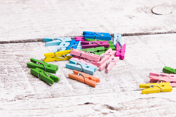 many multi-colored wooden small stationery decorative clothespins on a light wooden plank background, clothespins for notes