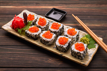 Sushi roll with red caviar on a plate with wasabi, ginger, maple leaves and chopsticks for sushi, on a wooden background