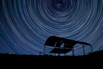 Digital composite image of star trails around Polaris with derelict barn silhouette