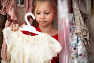 Little child girl choosing her clothes. Kid thinking what to choose to wear in front of many choices of dresses on hangers. Sales, buy and sell concepts. High quality photo