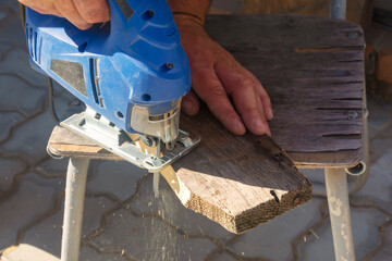 A man processes wood with an electric jigsaw. A carpenter sawing a board with a blue electric...