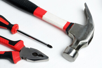 Screwdriver, hammer and pliers on a white wooden background