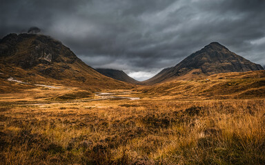 Autumn landscape in Glen Coe, Scotland, with dark clouds hanging over the peaks of Buachaille Etive Beag and Aonach Eagach.