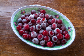 Closeup frozen cherries on a plate on a light wooden background