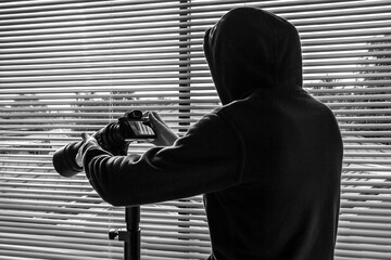 Man looks through blinds from a dark room and taking photos on the camera.