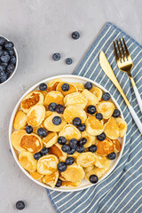 Trendy home breakfast with tiny pancakes and blueberry on gray concrete background. Flat lay, top view, overhead, mockup, template, copy space. View from above. High quality photo