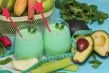 two glasses of vegetable smoothie with ribbon and vegetables on a blue background, closeup side view.